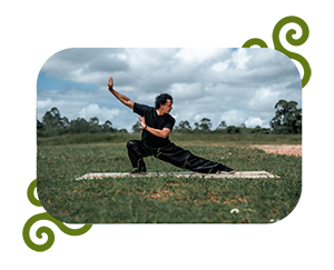 Homme pratiquant le Tai Chi en extérieur, en position de méditation avec les bras étendus et les jambes légèrement fléchies, entouré par la nature.